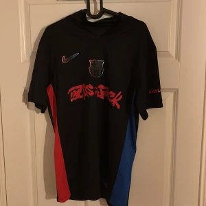 Fotbollströja  - Säljer en svart FC Barcelona x Cactus Jack fotbollströja från Nike med röd och blå detalj på sidorna. Tryck med Cactus Jack-logga på bröstet, FCB-emblem och Nike swoosh. På ryggen står Lamine Yamal och nummer 19. Använd fåtal gånger, nyskick 