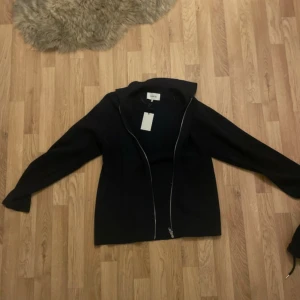 Mörkblå zip tröja med dragkedja från Norvie - Svart jacka från Norvie i storlek M. Jackan har en stilren design med lång ärm och hel dragkedja framtill. Perfekt för dig som gillar en enkel och clean look. Materialet känns mjukt och passar bra till lager-på-lager-stil.