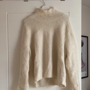 Krämvit polotröja i ullmix - Mysig krämvit polotröja med ribbad hög krage och långa ärmar. Tröjan är stickad i en mjuk ullmix och har en loose passform med ribbade muddar vid nederkant och ärmslut.