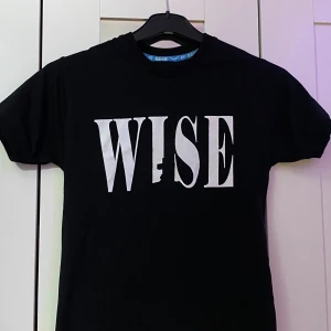 Svart t-shirt med WISE-tryck och schackmotiv - Svart t-shirt från B&SH med stort vitt WISE-tryck på bröstet och schackpjäser samt text på ryggen. Klassisk rund hals och korta ärmar. Materialet är mjuk bomull, perfekt för en cool och avslappnad look. Snygg T-shirt. Som ni ser på bilden så finns det ingen storlek på men jag kan säga att den verkar vara i storlek S eller så kan ni veta måttet istället. Höjden/längden är 61cm och bredden (från ena axeln till det andra) är 34cm. Meddela gärna för mer info! 💕