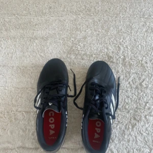 Adidas Copa Sense 4 fotbollsskor svart - Säljer ett par svarta Adidas Copa Sense 4 fotbollsskor med vita detaljer och klassiska ränder på sidan. Skorna har snörning och en greppig sula perfekt för konstgräs. Tillverkade i syntetmaterial och har en sportig, stilren look.