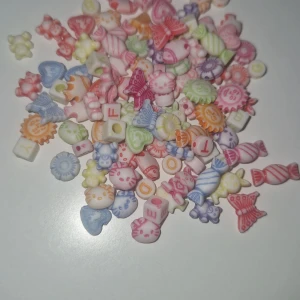 Färgglada pärlor till smyckestillverkning - Säljer ett mixat paket med söta pärlor i olika former som fjärilar, hjärtan, Hello Kitty, blommor och godisar. Pärlorna är i pastellfärger som rosa, blå, lila, grön, gul och orange. Perfekt för att göra egna armband, halsband eller örhängen. Kommer i en zip-påse.