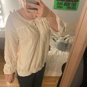 Vit prickig blus från Sally - Säljer en söt vit blus från Sally i storlek 40. Blusen har diskret prickigt mönster, rund hals med knappar och spetsdetaljer framtill. Ärmarna är långa med knyt vid mudden och nederkanten är smockad för en chill look. Perfekt för dig som gillar romantisk stil.