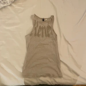 Beige ribbad linnetopp med tryck - Säljer en beige ribbad linnetopp från H&M med ett coolt tryck framtill. Plagget är i fint skick och har en tightare passform. Pris kan diskuteras 💕