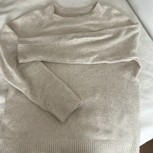 Beige stickad tröja från Vero Moda - Mysig beige stickad tröja från Vero Moda med rund halsringning och ribbade muddar vid ärmslut och nederkant. Perfekt för lager-på-lager och enkel att matcha med jeans eller kjol.