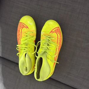 Neongula Nike fotbollsskor - Säljer ett par riktigt coola neongula Nike fotbollsskor med röda detaljer och snörning. Skorna har en smal passform och är tillverkade i syntetmaterial för bästa grepp och känsla på planen. Perfekta för dig som vill sticka ut och dominera på fotbollsplanen.