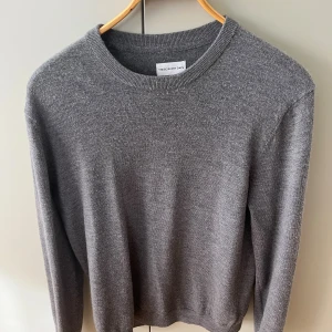 Grå merinoulltröja These Glory Days - Säljer en stilren grå stickad tröja från These Glory Days i mjuk merinoull. Tröjan har rund halsringning, ribbade muddar och lång ärm. Perfekt för lager-på-lager och funkar året runt. Enkel att matcha med jeans eller chinos.