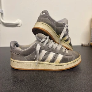 Ljusgråa Campus 00s - De finns många täcken på användning och defekter som grönska (bild 2), missfärgningar och nötta i hälen (inget som känns eller syns vid användning). Tillkommer oanvända gråa snören till. Nypris ligger runt ca 1000kr