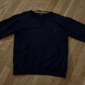 Mörkblå sweatshirt från Replay - Säljer en stilren mörkblå sweatshirt från Replay med röd broderad R på bröstet. Tröjan har rund halsringning, långa ärmar och ribbade muddar. Perfekt för dig som gillar enkel och snygg streetstil.