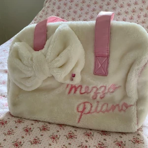 Mezzo Piano fluffig väska med rosett  - Supergullig fluffig väska från Mezzo Piano! Köp i Japan. Väskan är i vit pälsimitation, har en stor söt rosett framtill och broderad logga i rosa. Perfekt för skola eller gymväska! 