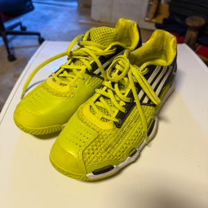 Adidas gula innomhussskor - Säljer ett par sportiga sneakers innomhusskor från Adidas i en riktigt cool gul färg med svarta och vita detaljer. Skorna har ventilerande mesh, syntetiska partier och klassiska ränder på sidan. Platt sula med bra grepp och snörning framtill. Perfekta för dig som gillar att sticka ut. Haft dom på få innebandyträningar 
