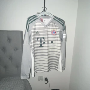 Bayern München långärmad målvaktströja - Säljer en långärmad Bayern München målvaktströja från Adidas i grått och vitt med horisontella ränder. Tröjan har klubbmärke på bröstet, gröna axelränder och är tillverkad i lätt och ventilerande Climalite-material.