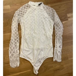 Vit spetsbody med lång ärm - Säljer en vit spetsbody med långa ärmar och hög hals. Använd en gång. Storlek M/38.