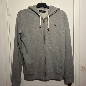 Grå hoodie med dragkedja från Morris - Grå hoodie från Morris med dragkedja, huva och vita snören, den är som ny och använd fåtal gånger.