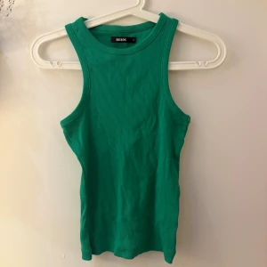 Grön ribbad linnetopp från Bik Bok - Snygg grön linnetopp från Bik Bok i storlek S. Toppen är ribbad och har en ärmlös design med rund halsringning. Perfekt för dig som gillar en enkel men fräsch look. Materialet är mjukt och stretchigt.