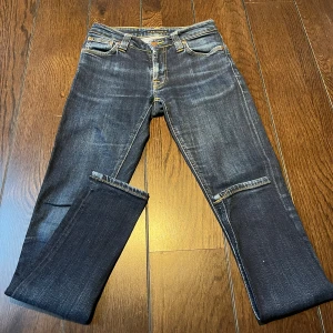 Mörkblå jeans från Nudie Jeans 27/32 - Snygga mörkblå jeans från Nudie Jeans med klassisk femficksdesign och kontrastsömmar. Bakfickorna har Nudie Jeans ikoniska broderi i orange. Jeansen har en smal passform och är tillverkade i slitstarkt denimtyg.