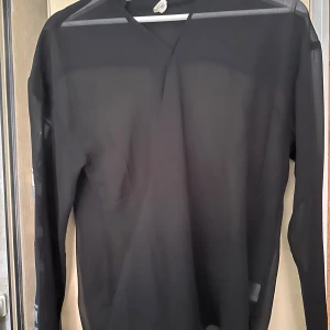 Svart omlottblus från Uniq Young - Snygg svart omlottblus från Uniq Young i transparent och lätt material. Blusen har lång ärm och en stilren v-ringad hals. Perfekt för dig som gillar en clean och modern look. Passar dig som vill ha något enkelt men ändå trendigt.