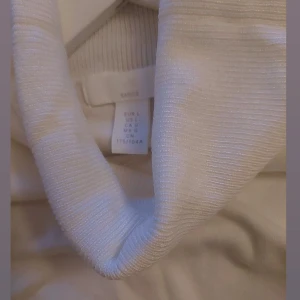 Vit styckade polotröja från H&Mi storlek L - Klassisk styckade vit polotröja från H&M  i storlek L. Tröjan har lång ärm, ribbade muddar och hög polokrage. Perfekt att styla lager på lager eller bära som den är. Materialet är mjukt och stretchigt för en bekväm passform.