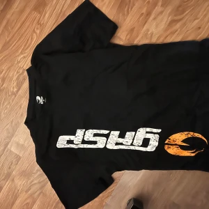 Svart t-shirt med tryck från GASP - Svart t-shirt från GASP med stort vitt och orange tryck på framsidan. Oanvänd. Vill ba bli av med tröjan.