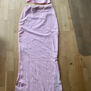 Ljusrosa långkjol i bomull med en topp till - Långkjol i ljusrosa med en topp till med enkel, rak passform och mjukt bomullstyg. Kjolen har en slits på sidan och är helfärgad utan mönster. Perfekt för dig som gillar en clean och feminin look. aldrig använt innan, kjolen är väldigt genomskinlig. från shein