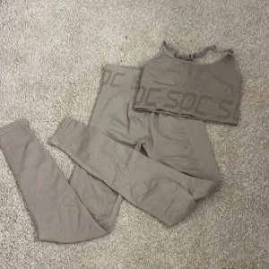 Beige ribbad linnetopp från SOC - Säljer en beige ribbad linnetopp från SOC med breda axelband och logga längs nederkanten. Toppen är stretchig och gjord i mjukt syntetmaterial, perfekt för träning. Snygg och enkel design som är lätt att matcha med leggings eller shorts.med matchande byxor till, kan diskutera priset 💗