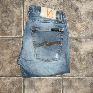 Nudie Jeans - Snygga blå jeans från Nudie Jeans, modellen Tight Long John. De har en slim och tight passform med klassisk femficksdesign, orangea sömmar och broderad detalj på bakfickorna. Materialet är bomull med lite stretch för extra komfort. Midja 36, längd 102cm. Ifall det inte finns någon bild i annonsen där jag bär plaggen jag säljer så är det för att jag ej kan ha storleken heller passformen, så kolla måtten för storlek och googla på modellnamnet för passform 😉 s4