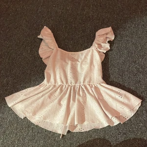 Ljusrosa topp med volang från SHEIN - Supersöt ljusrosa topp från SHEIN i storlek XS. Toppen har volangärmar, broderade detaljer och snörning i ryggen. Materialet är lätt och känns som bomull, perfekt för varma dagar. Den har ett romantiskt mönster med små hål och en söt, utställd kjol.