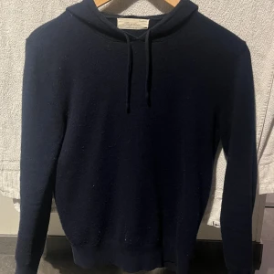 Marinblå cashmere hoodie från Sayleas - Mjuk och lyxig mörkblå hoodie från Sayleas i 100% cashmere. Tröjan har huva med snörning och långa ärmar, perfekt för dig som gillar stilren och enkel design. Ribbstickade muddar vid ärmslut och nederkant ger en snygg passform.