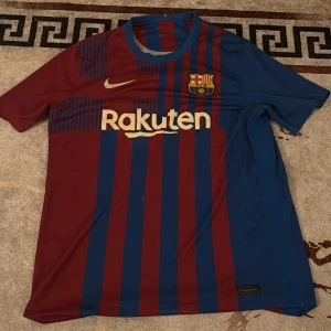 FC Barcelona kortärmad matchtröja Nike - Säljer en FC Barcelona fotbollströja från Nike med klassiska röda och blå vertikala ränder, klubbmärke på bröstet och Rakuten-logga. Tröjan är kortärmad och har rund hals. Perfekt för dig som älskar Barca och vill ha en snygg matchtröja i polyester.