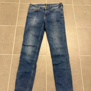 Blå Lee jeans W28 L33 - Snygga blå jeans från Lee. Klassisk femficksdesign, gul kontrastsöm och Lee-logga på bakfickan. Jeansen har normal midja och är tillverkade i stretchigt bomullsmaterial för skön passform.