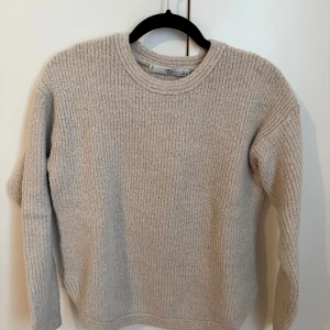 Beige stickad tröja från MNG - Mysig beige stickad tröja från MNG Basics i storlek S. Tröjan har ett ribbat mönster, rund halsringning och långa ärmar. Perfekt för dig som gillar enkel och stilren design med en soft vibe. Passar dig som vill ha en basic men ändå snygg tröja.