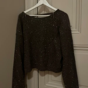 Glittrig mörkgrå stickad tröja Gina Tricot - Snygg mörkgrå stickad tröja från Gina Tricot Young med glittriga detaljer. Tröjan har lång ärm och en rak, lite croppad passform. Perfekt för dig som vill ha en enkel men ändå festlig look med lite extra glitter.