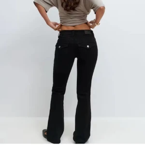 Svarta bootcut jeans från Perfect Jeans - Snygga svarta jeans från Perfect Jeans med bootcut-modell och låg midja. Jeansen har silverfärgade knappar på bakfickorna och är tillverkade i stretchigt denimtyg för en bekväm passform. Perfekta för dig som gillar en klassisk men trendig look.