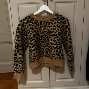 Leopardmönstrad stickad tröja från Zara - Säljer en snygg stickad tröja från Zara med leopardmönster i beige, svart och vitt. Tröjan har rund halsringning, ribbade muddar och är långärmad. Perfekt för dig som vill sticka ut med en trendig look.