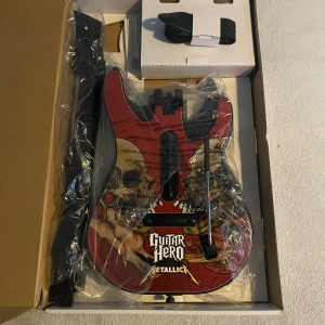 Guitar Hero Metallica Gitarrkontroller - Guitar Hero Metallica gitarrkontroller i originalkartong, ser oanvänd ut med plasten kvar på delarna. Inkluderar två utbytbara kroppar (Metallica och sunburst), hals, rem och tillbehör. 