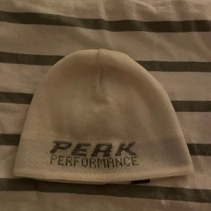 Vit mössa Peak Performance - Snygg vit mössa från Peak Performance med logotypen broderad framtill. Enkel och stilren design som passar perfekt för kalla dagar. Mjuk och skön kvalitet, perfekt för dig som gillar sportiga och cleana accessoarer.