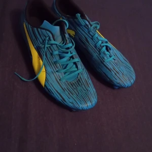 Puma fotbollsskor  - Säljer ett par snygga blå fotbollsskor från Puma i storlek 45. Skorna har coolt randigt mönster i svart och blått, gula detaljer och klassisk Puma-logga. Utrustade med dobbar för gräsplan och snörning för bra passform. Perfekta för dig som vill sticka ut på planen.