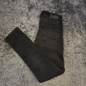 Svarta Lee Luke jeans W28 L32 - Säljer ett par svarta Lee Luke jeans i storlek W28 L32. De har en slim passform med smalare ben och klassisk femficksdesign. Jeansen är tillverkade i bomull med lite stretch för extra komfort. Snyggt Lee-märke bak i midjan och diskreta slitningar för en cool look. Helt oanvända!!!! Slim fit!!!