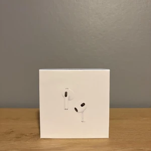 AirPods 3 - Säljer ett par AirPods 3 i nyskick med originalförpackning, laddningsetui och USB-C kabel. Hörlurarna är trådlösa och har aktivt laddningsetui med LED-indikator. Inga synliga repor eller slitage, allt ser ut som nytt. Perfekt för musik, samtal och träning.