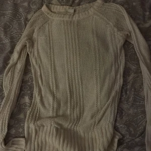 Beige stickad tröja från Vila - Säljer en beige stickad tröja från Vila med snyggt strukturmönster och ribbade muddar. Tröjan har lång ärm och rund halsringning, perfekt för lager på lager under kyliga dagar.