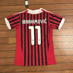 AC Milan Ibrahimovic tröja Adidas S - Säljer en officiell AC Milan fotbollströja från Adidas med Ibrahimovic och nummer 11 på ryggen. Tröjan är röd och svart med vertikala ränder, vita detaljer vid krage och ärmslut samt klubbmärke och Fly Emirates-logga på bröstet. Tillverkad i lätt polyester.