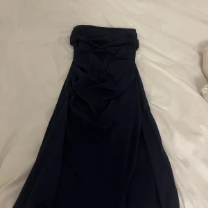 Marinblå axelbandslös långklänning - Säljer en stilren marinblå långklänning med axelbandslös design och snygg slits på sidan. Klänningen har en figurnära passform och är perfekt för dig som gillar minimalistisk och elegant stil. Materialet känns mjukt och följsamt mot kroppen.