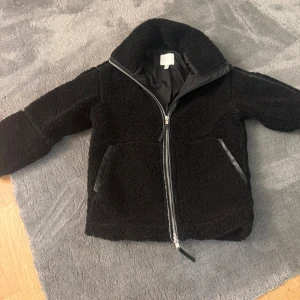 Svart teddyjacka med dragkedja - Mysig svart teddyjacka med stor krage och sned dragkedja framtill. Jackan har två fickor med snygga detaljer i svart och är helfodrad på insidan. Perfekt för dig som gillar en chill och trendig look under höst och vinter. Stl xxs/xs passar en som brukar ha 34/36järre fint skick 