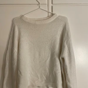 Vit stickad tröja - Säljer en enkel och stilren vit stickad tröja med rundad hals och långa ärmar. Tröjan har ribbade detaljer vid halsringning och nederkant, perfekt för att hålla värmen under kyliga dagar. Passar dig som gillar en clean och klassisk look.