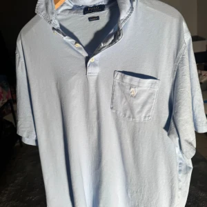 Ljusblå Polo Ralph Lauren henley - Fräsch ljusblå henley från Polo Ralph Lauren med klassisk krage, korta ärmar och bröstficka med broderad logga. Skjortan är i mjuk bomull och har knappar vid halsen för en chill look. Perfekt för dig som gillar stilren och enkel design. Vet inte riktigt storlek då för att storleks lappen är borta skulle gissa på L eller M 