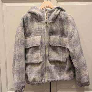 Mysig vinterjacka från Pull&Bear - Mysig vinterjacka från Pull&Bear. Jackan är fodrad med en mjuk utsida. Färgen är grå-rutig med hintar av lila. Använd endast ett fåtal gånger. Normal i storlek.
