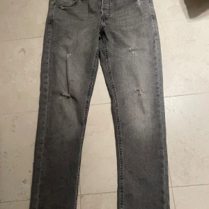 Grå slim jeans Jack & Jones Glenn - Grå jeans från Jack & Jones i modellen Glenn med slim passform. Byxorna har slitna detaljer på benen och klassisk femficksdesign. Tillverkade i mjukt denimtyg som ger en skön känsla och snygg look.
