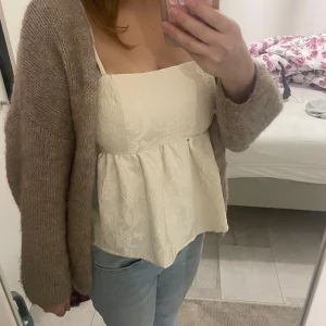 Vit blommig linnetopp med volang - Supersöt vit linnetopp med diskret blommigt mönster och volang nedtill. Toppen har breda axelband och fyrkantig ringning, vilket ger en trendig och romantisk look. Perfekt att styla med jeans eller kjol för en fräsch vibe. S/M