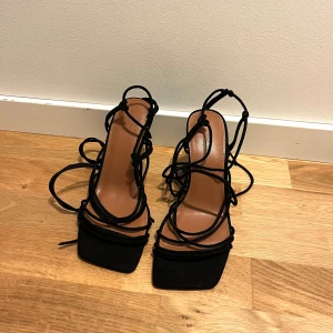Svarta klackar ASOS Design 39  - Svarta sandaletter från ASOS DESIGN med höga klackar och trendiga snörningsdetaljer som går att knyta vid fötterna på eller på vaderna. Bekväma och lätta att gå i, storlek 39 