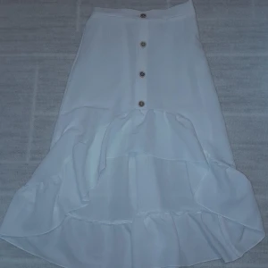 Vit volangkjol med knappar från SHEIN - Supersöt vit långkjol från SHEIN med volangdetaljer och knappar framtill. Kjolen har en flowy känsla och är tillverkad i ett lätt syntetmaterial som ger en luftig look. Skriv för frågor osv!💕 (Endast swish)